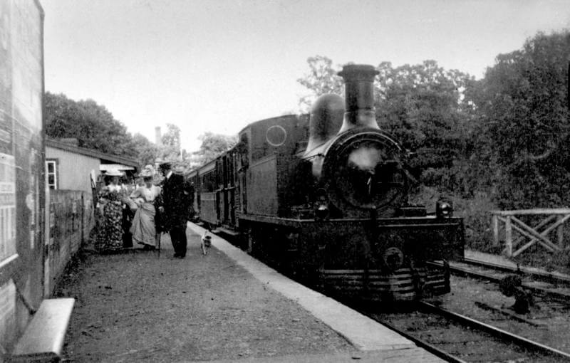 Vintage black and white photograph of a steam train at a station platform with people around.