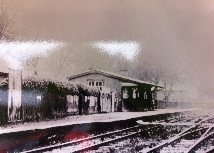 Old black and white photograph of a small building by train tracks with snow on the ground.